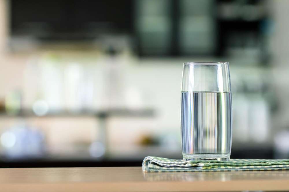 A clear glass of water on a kitchen counter with a blurred modern kitchen background, symbolizing safe and treated household water