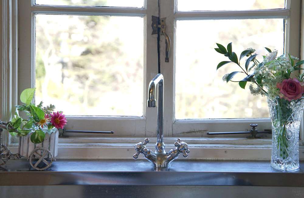 A farmhouse kitchen sink with flowers on the counter in vases to the right and left.