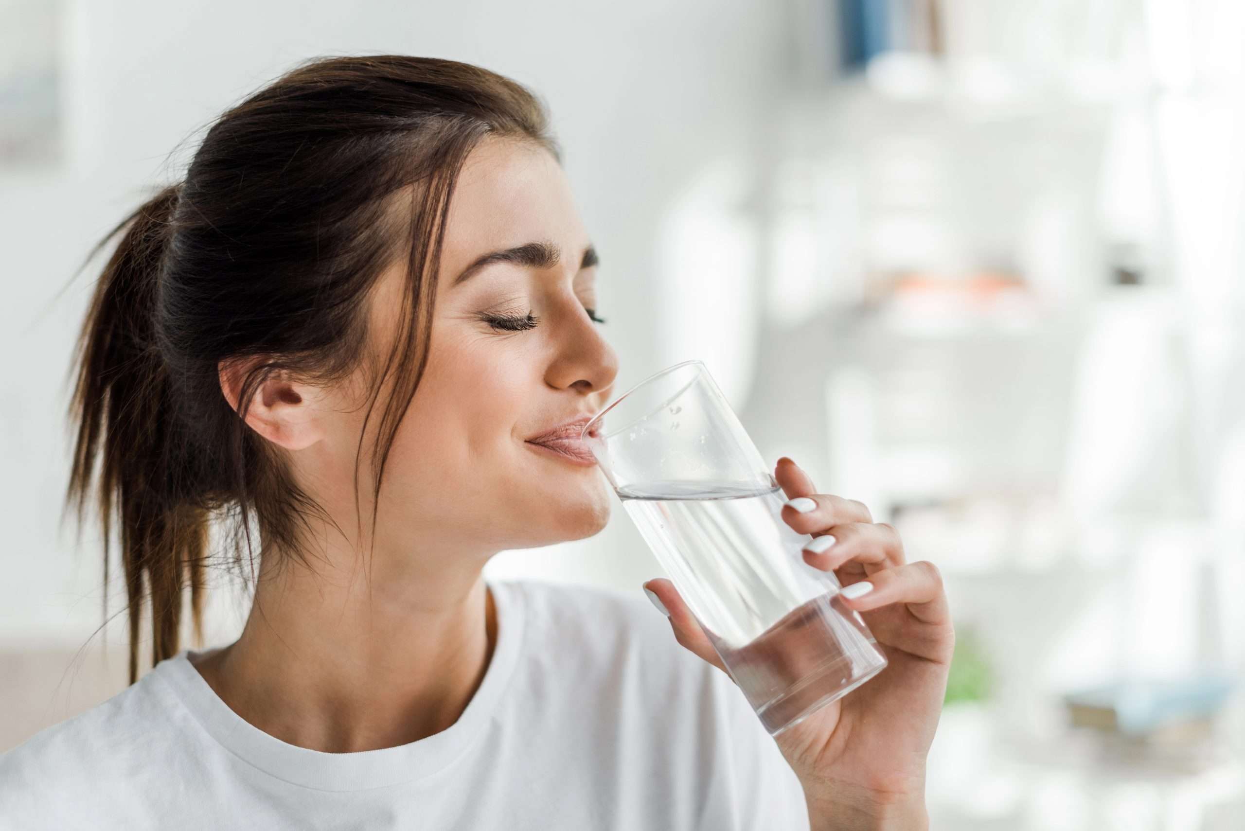 A woman happily drinking a clear glass of water.